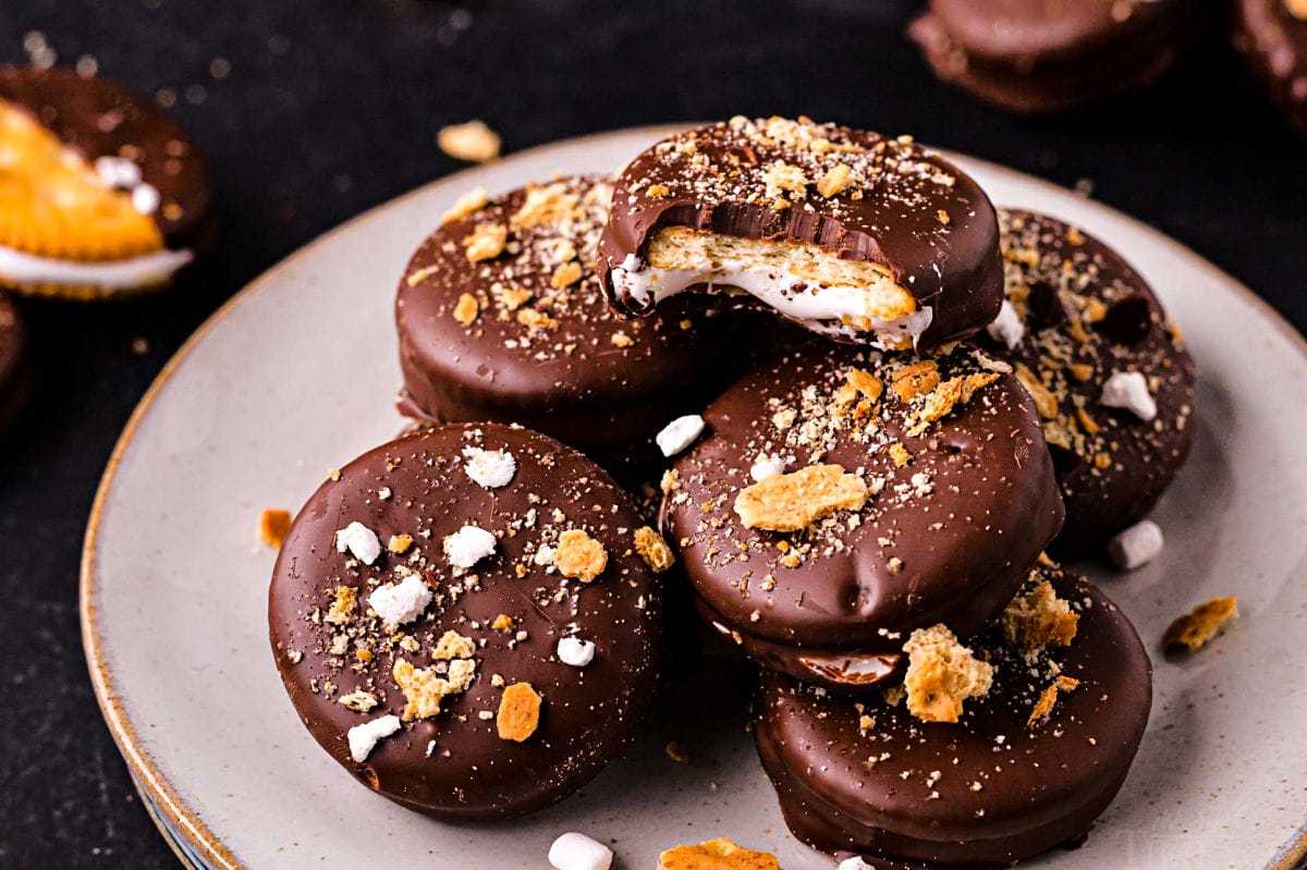 plate of chocolate dipped ritz sandwich cracker smores cookies. cookies are topped with crushed graham crackers and marshmallow bits as well as mini chocolate chips.