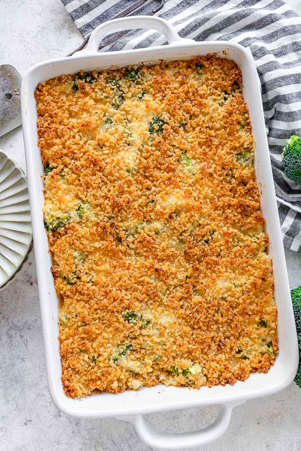 top down look at broccoli rice cheese casserole in a white baking dish next to a black and white striped towel.
