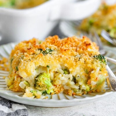 serving of broccoli rice casserole on a small decorative white plate with the casserole dish in the background.