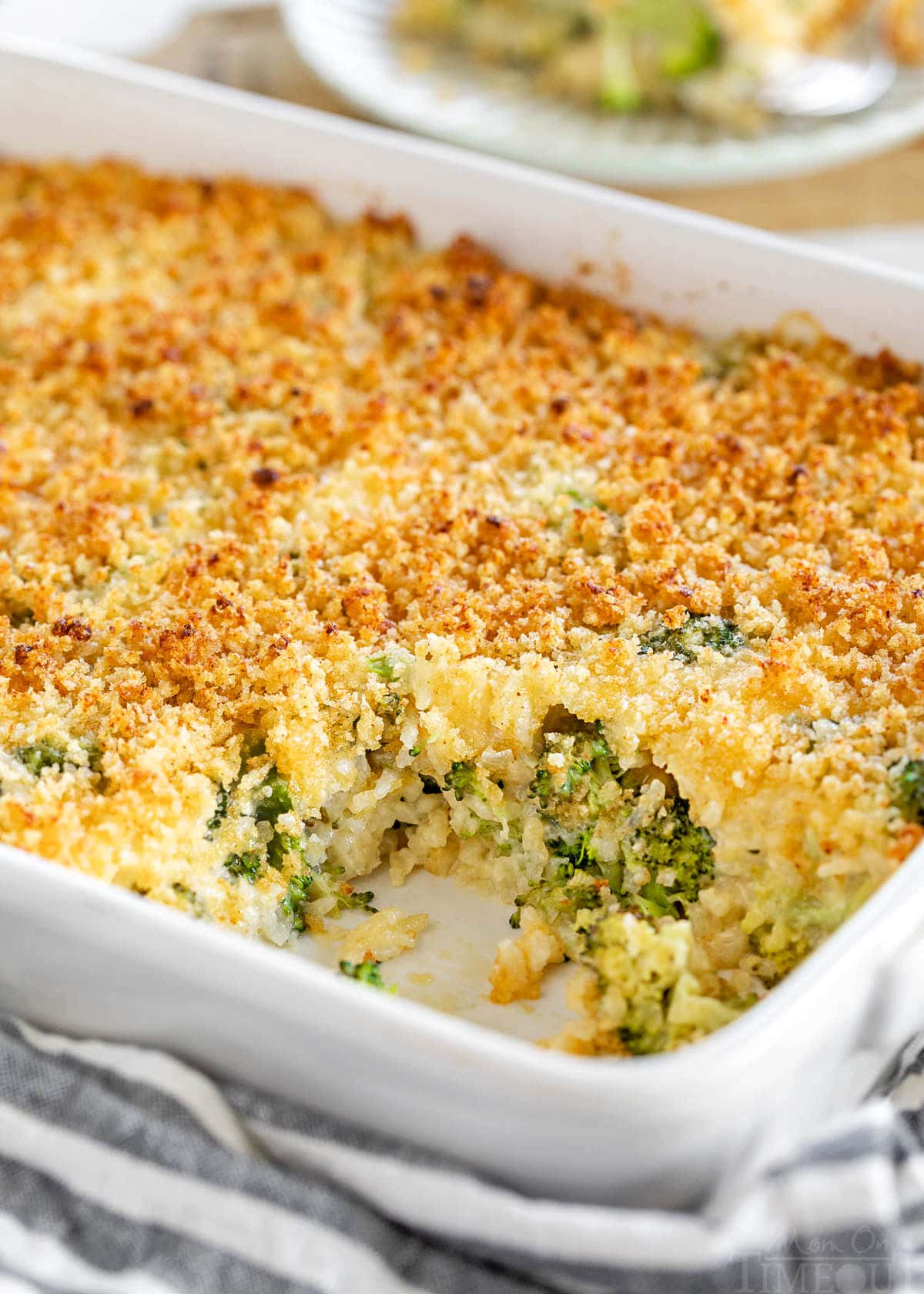 white casserole dish with broccoli rice casserole recipe in it. scoop of the casserole has been removed and is on a small white plate in the background.