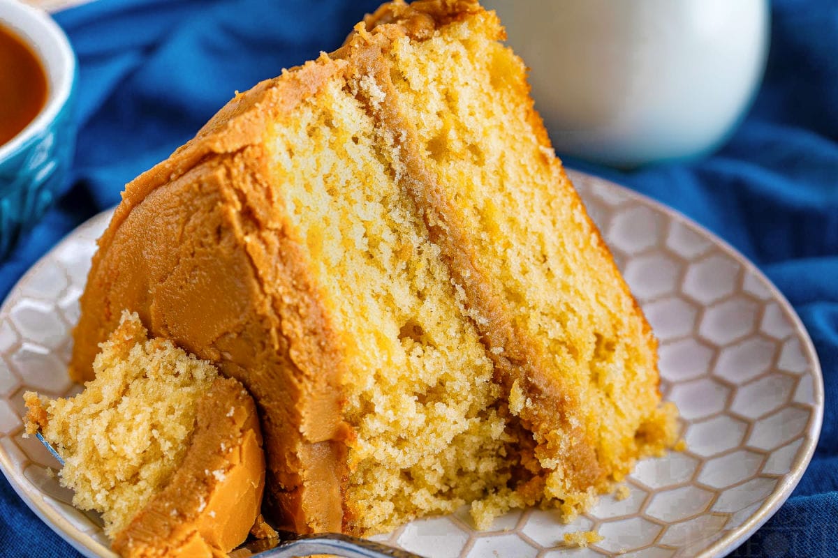 slice of caramel layer cake on a white plate with a forkful of cake resting on the side of the plate.