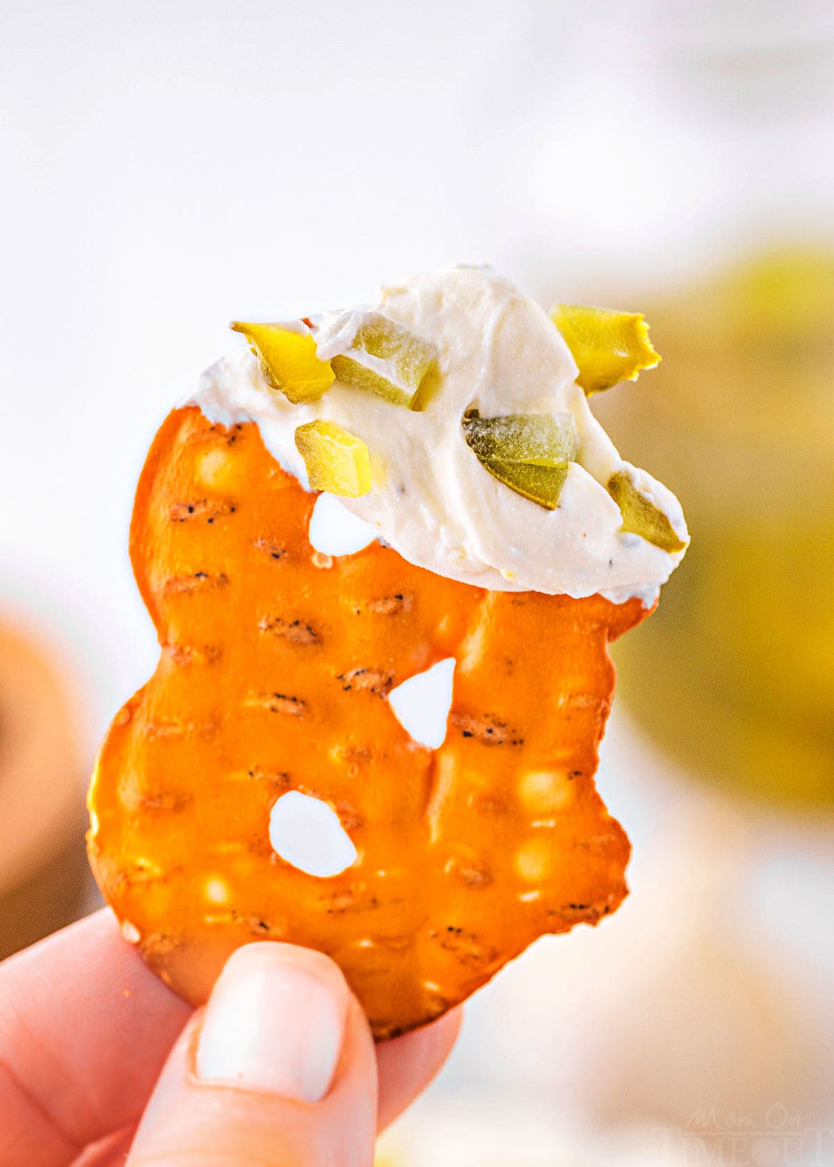 pretzel chip is being held up with dill pickle dip on the end of the pretzel.
