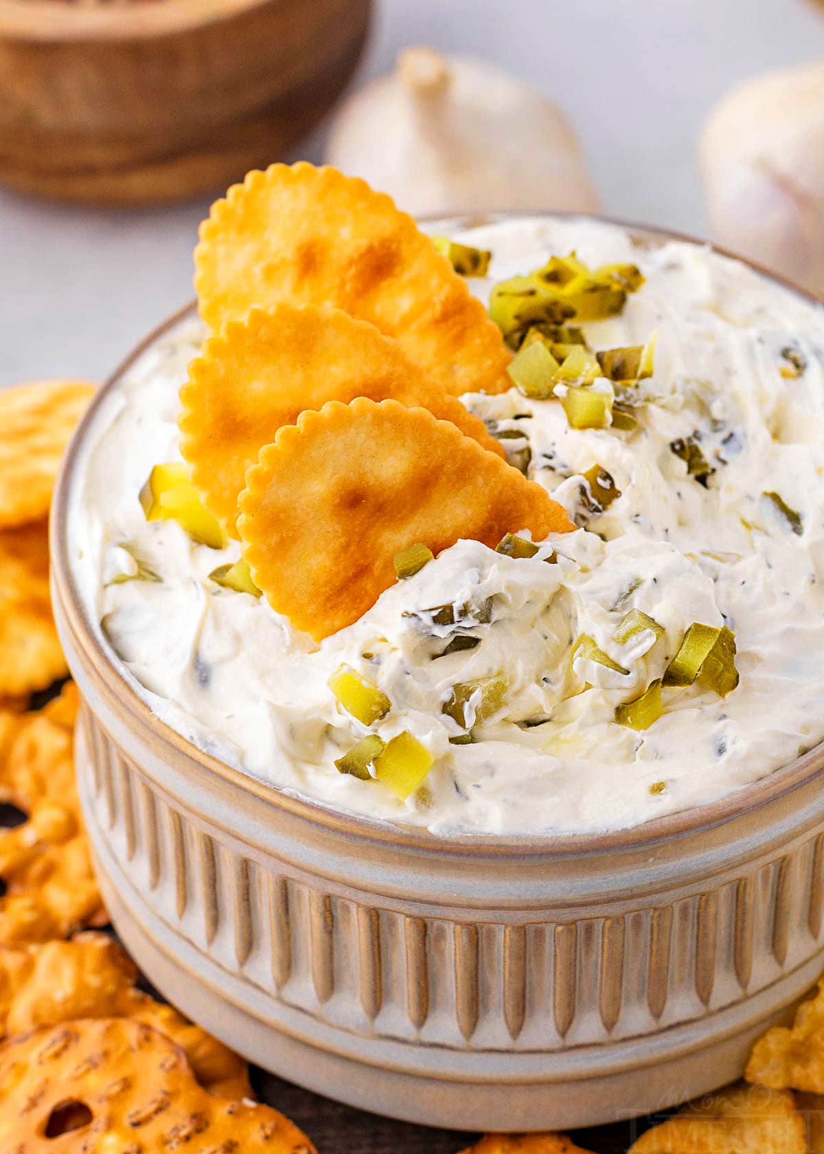 small clay bowl with dill pickle dip in it. three crackers are dipped into the dip with a sprinkle of chopped pickle scattered on top. 