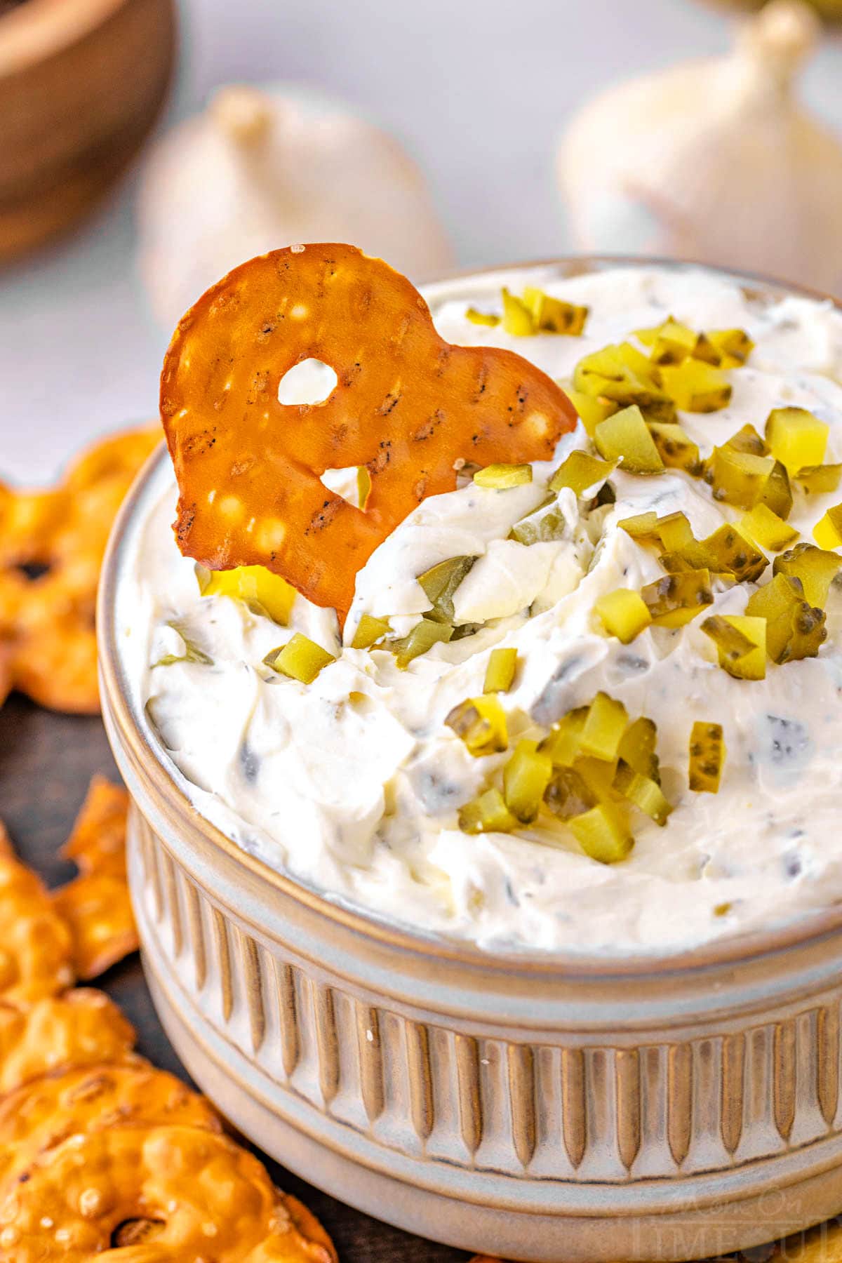 pretzel chip being dipped into a small bowl filled with pickle dip. 