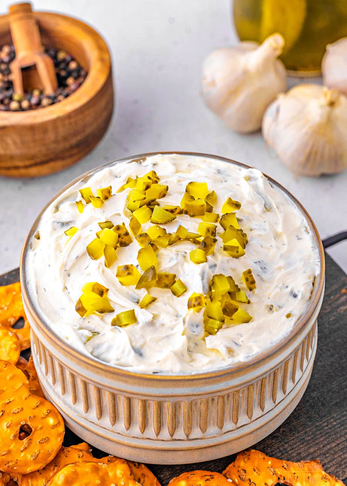 small decorative gray clay bowl with ridged detailing is filled with pickle dip and topped with more diced pickles. pretzels and chips surround the bowl.