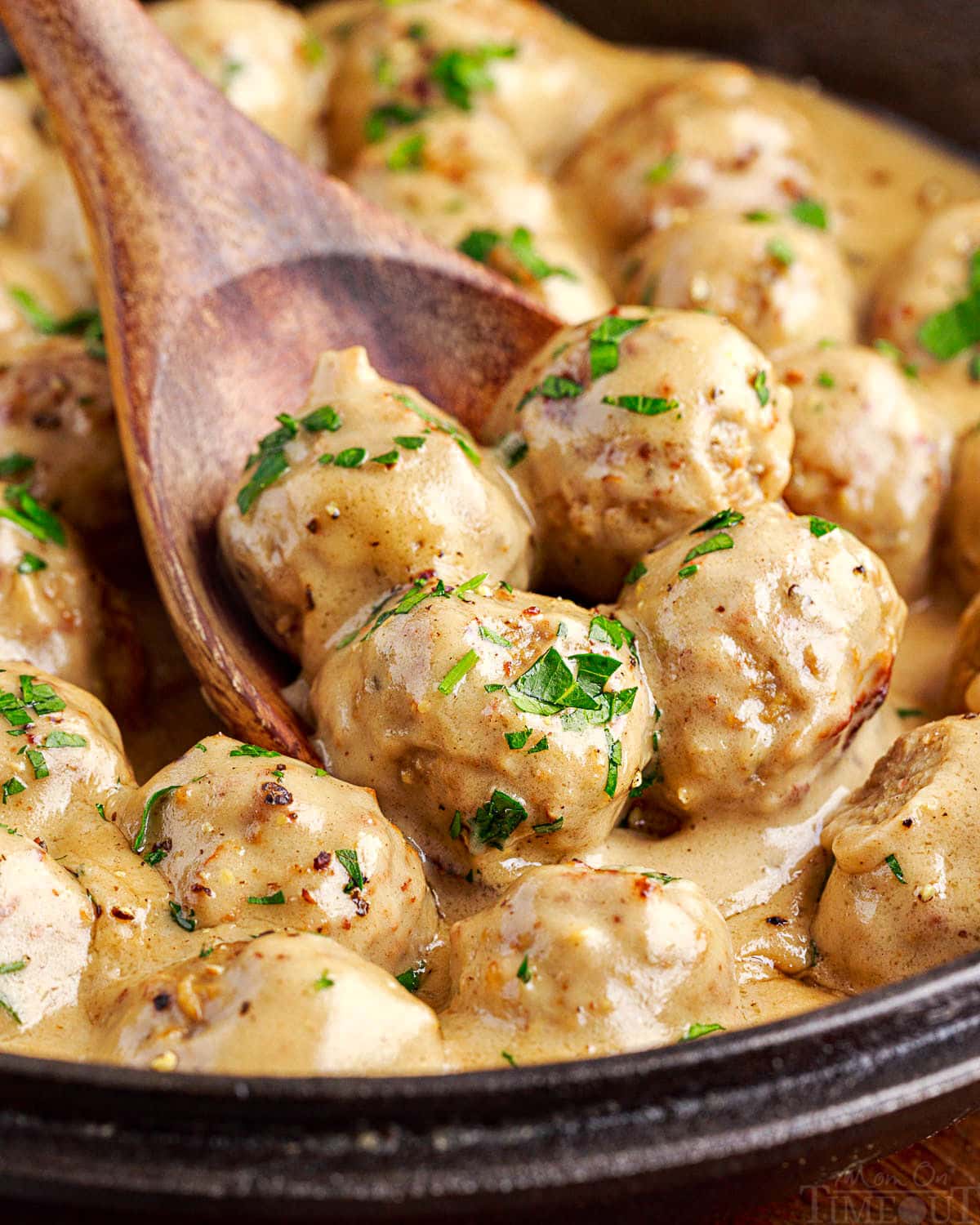 four meatballs on a wooden spoon being scooped out of skillet with the rest of the swedish meatballs and sauce.