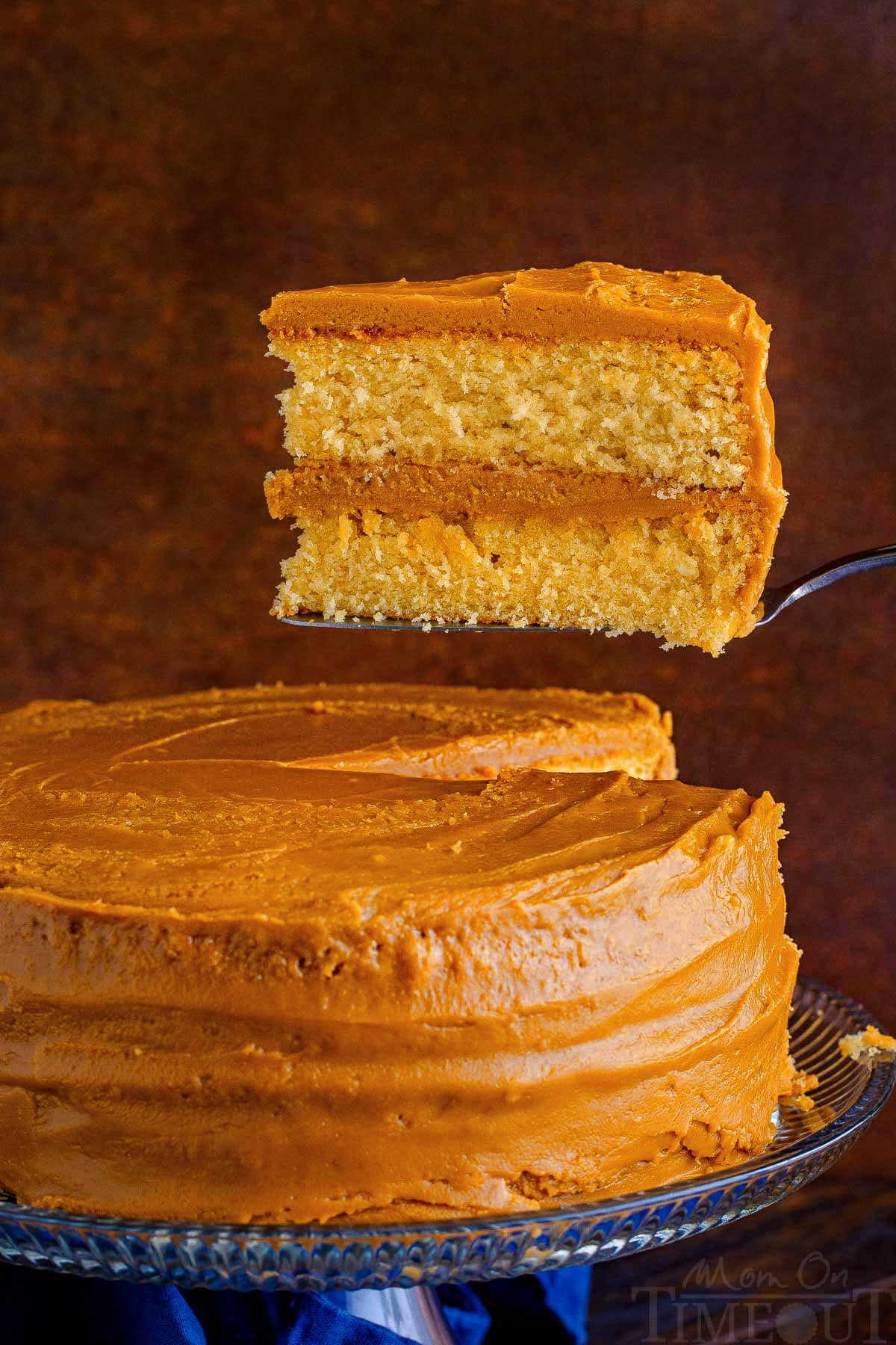 slice of caramel cake held above the rest of the cake sitting on a cake stand.