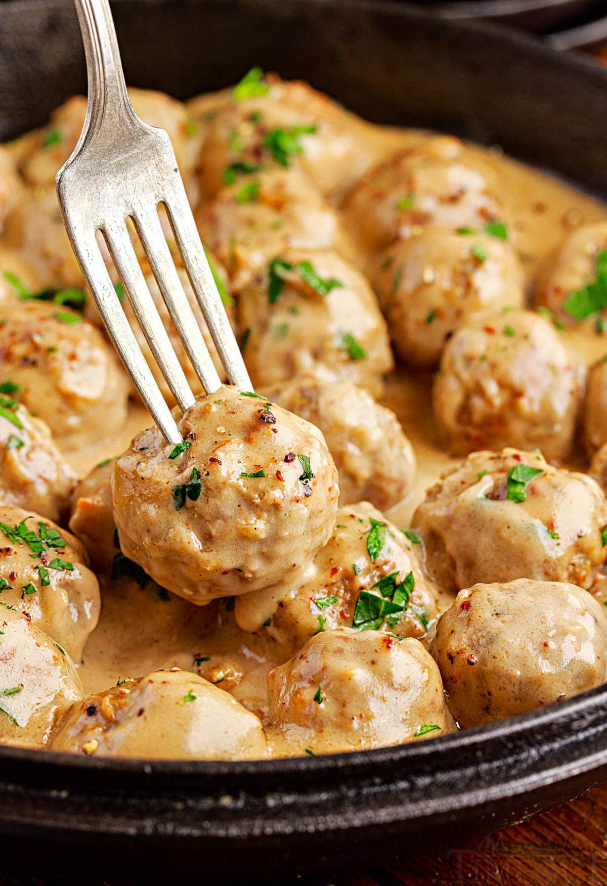 fork picking up a swedish meatballs out of a cast iron skillet.