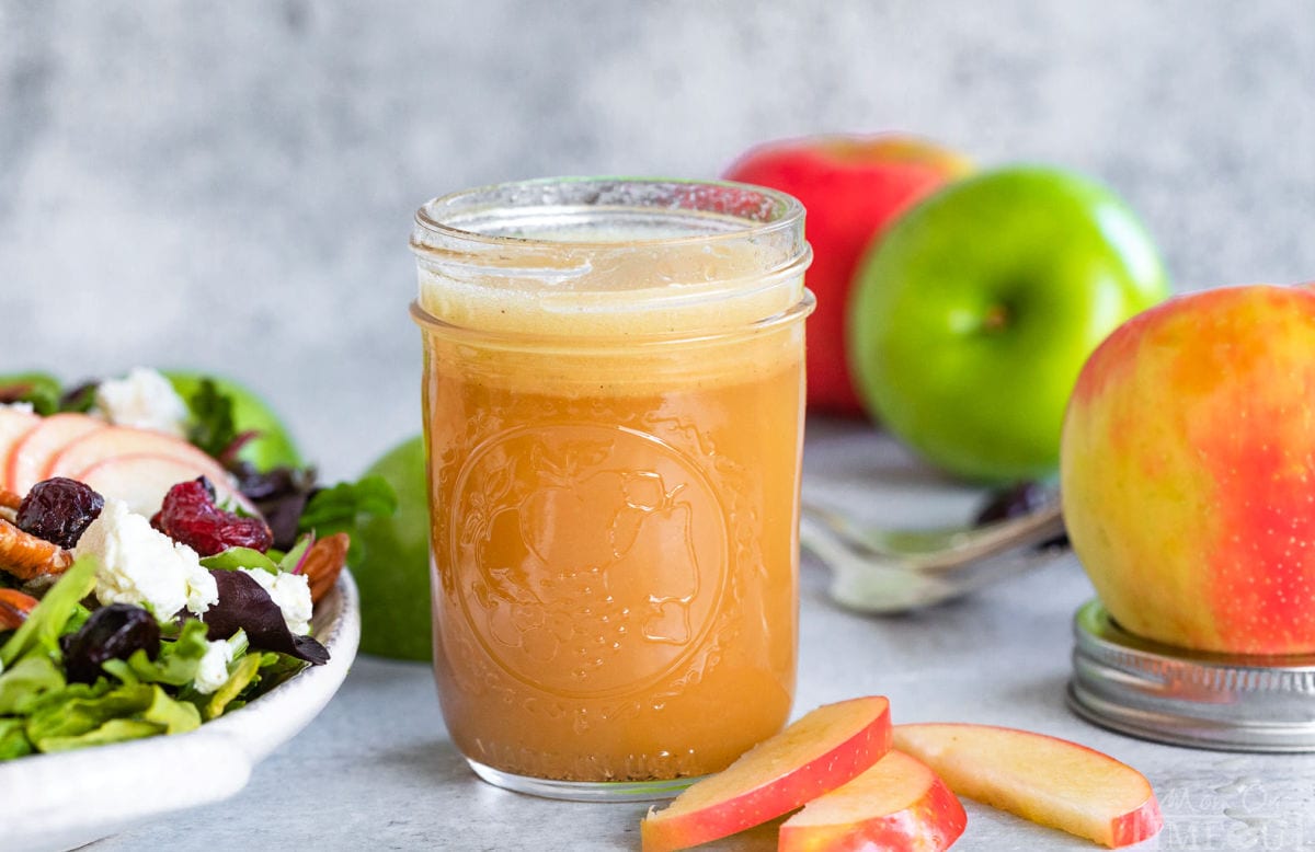 apple vinaigrette in small mason jar sitting next to a salad with apples in background.