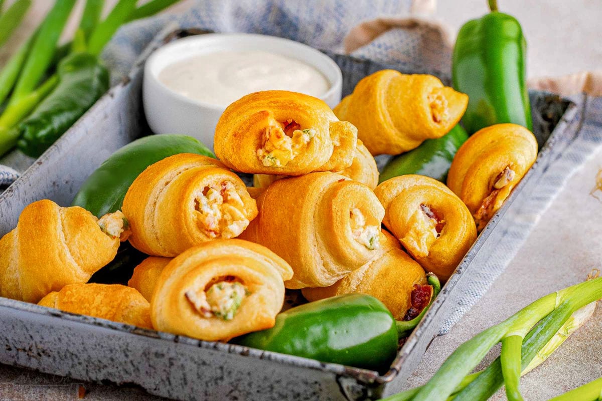 wide shot of jalapeno popper crescent rolls and fresh jalapenos. a small bowl of dip can be seen in the background.