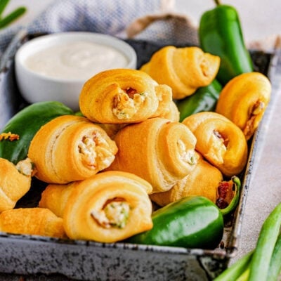 shot of jalapeno popper crescent rolls and fresh jalapenos. a small bowl of dip can be seen in the background and a white and blue towel.