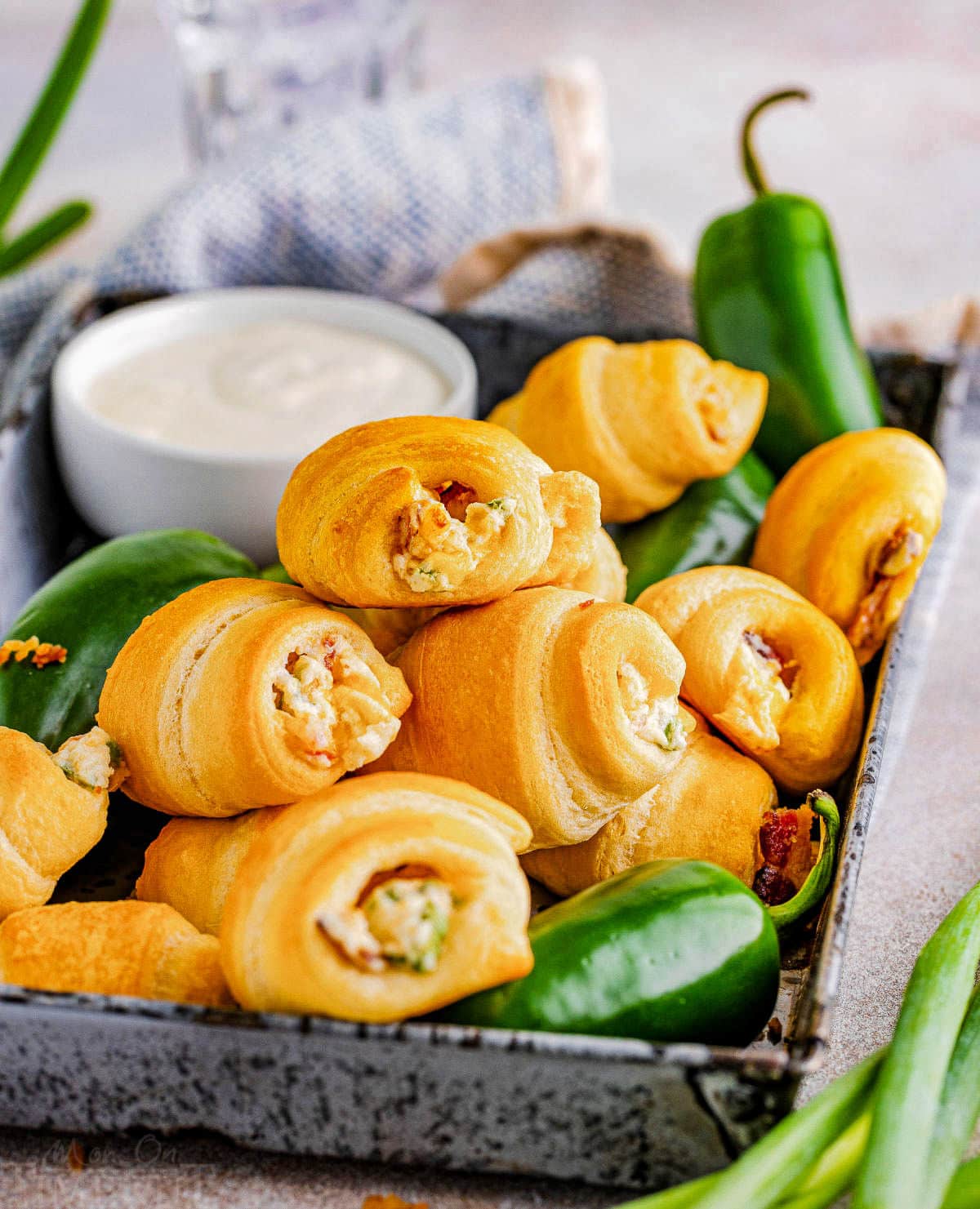 shot of jalapeno popper crescent rolls and fresh jalapenos. a small bowl of dip can be seen in the background and a white and blue towel.