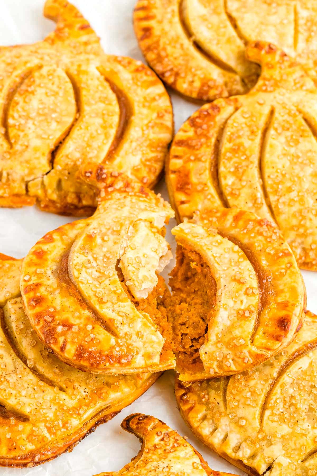 pumpkin hand pie split in half so you can see the pumpkin filling sitting on a plate with more pumpkin pies.