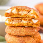 pumpkin snickerdoodle cookies stuffed with cheescake filling stacked on top of each other with the top cookie torn in half so you can see the filling.