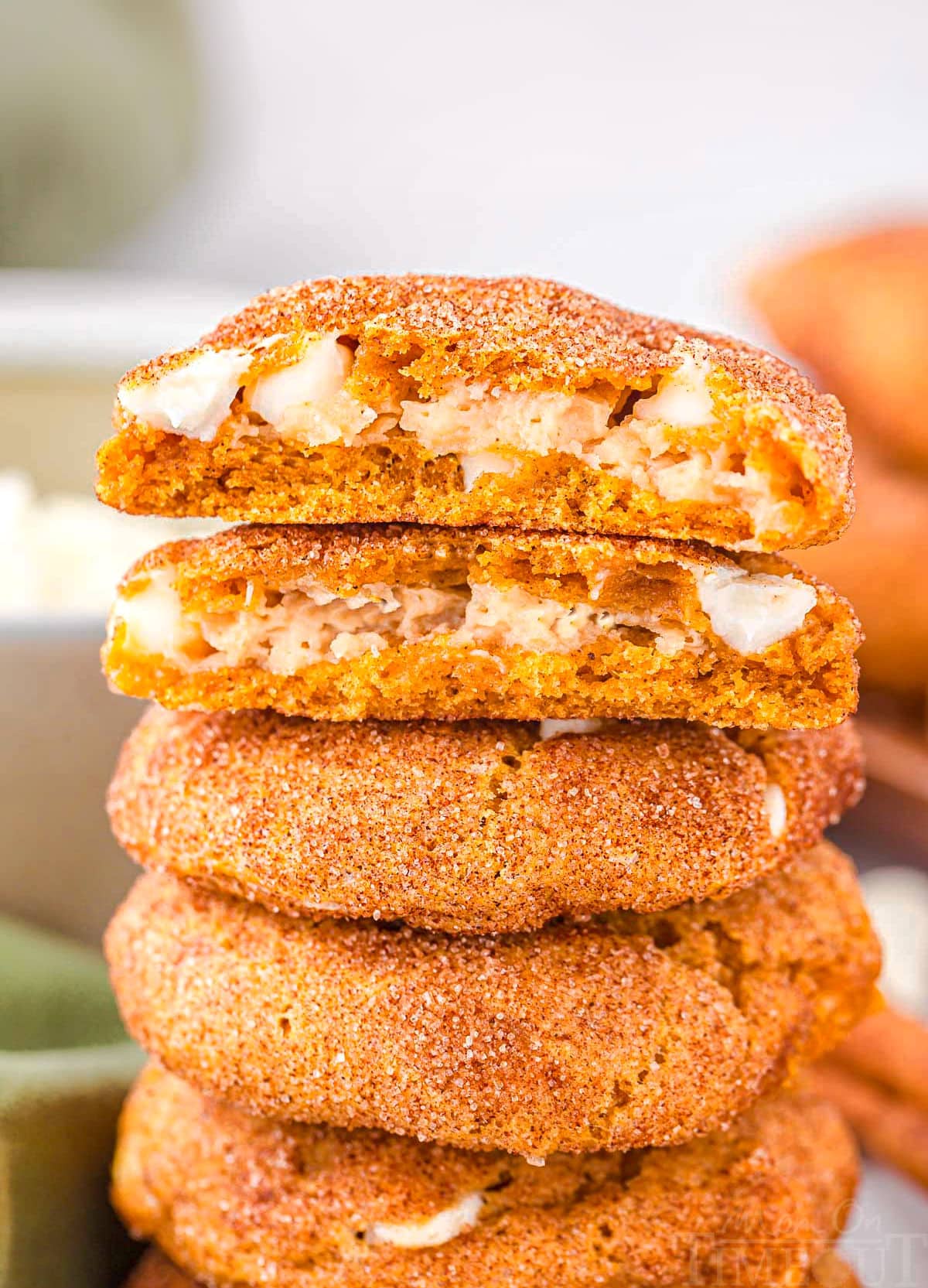 pumpkin snickerdoodle cookies stuffed with cheescake filling stacked on top of each other with the top cookie torn in half so you can see the filling.