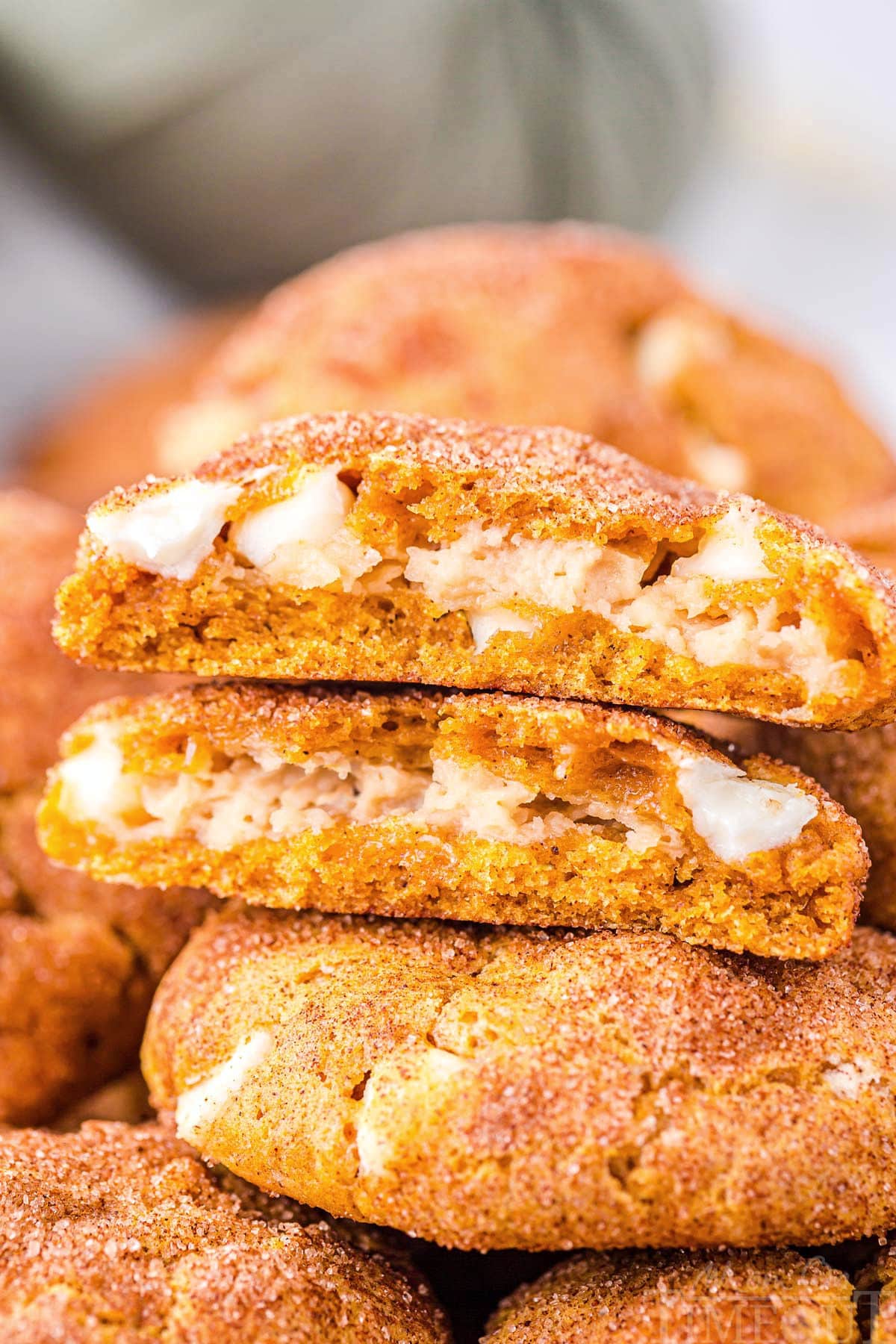 pumpkin snickerdoodle cookies stuffed with cheescake filling stacked on top of each other with the top cookie torn in half so you can see the filling.