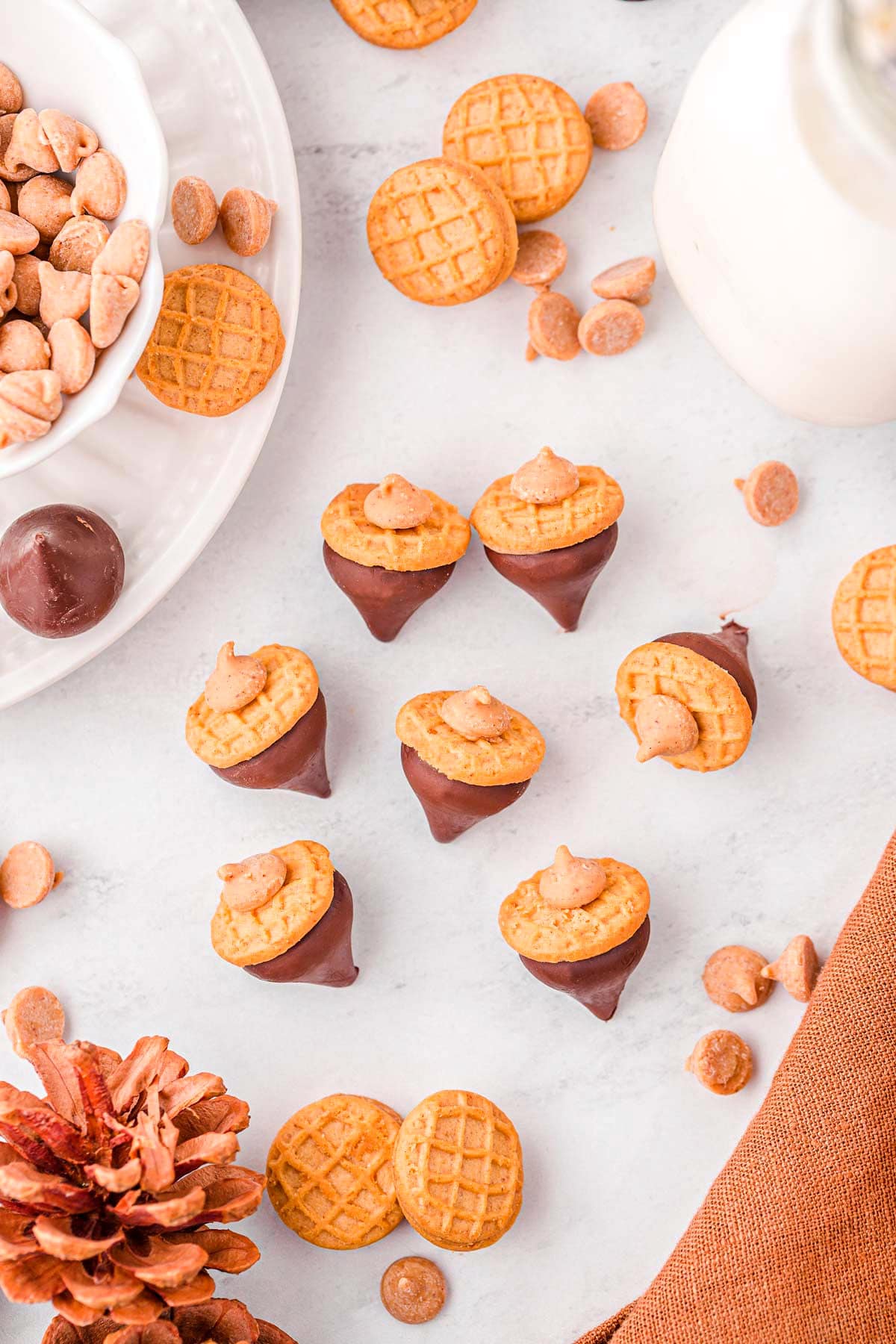 top down view of acorn cookies scattered on marble surface with a pinecone and brown napkin to the side.