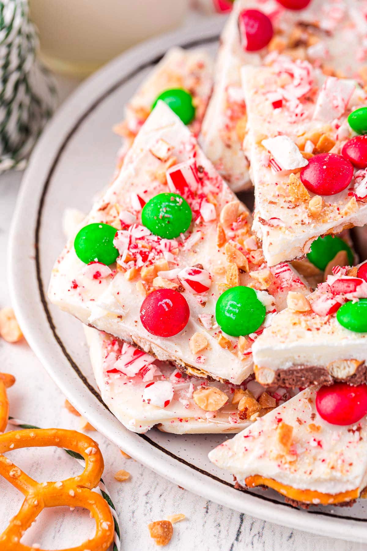 christmas candy bark on a white plate. the bark is decorated with christmas candy and made with pretzels.