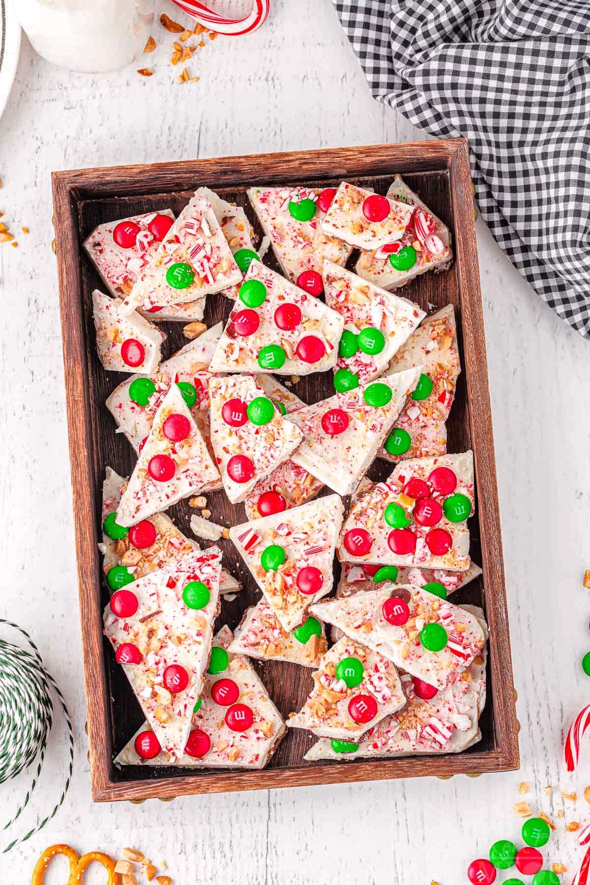 top down look at a lot of christmas decorated chocolate bark in a dark wooden tray.