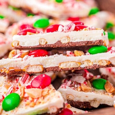 top down look at pieces of chocolate bark layered in a shallow wood tray. bark is decorated for christmas.