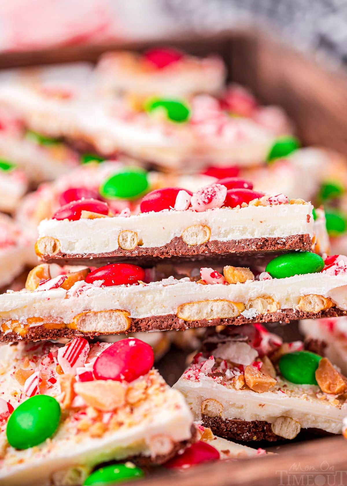 top down look at pieces of chocolate bark layered in a shallow wood tray. bark is decorated for christmas.