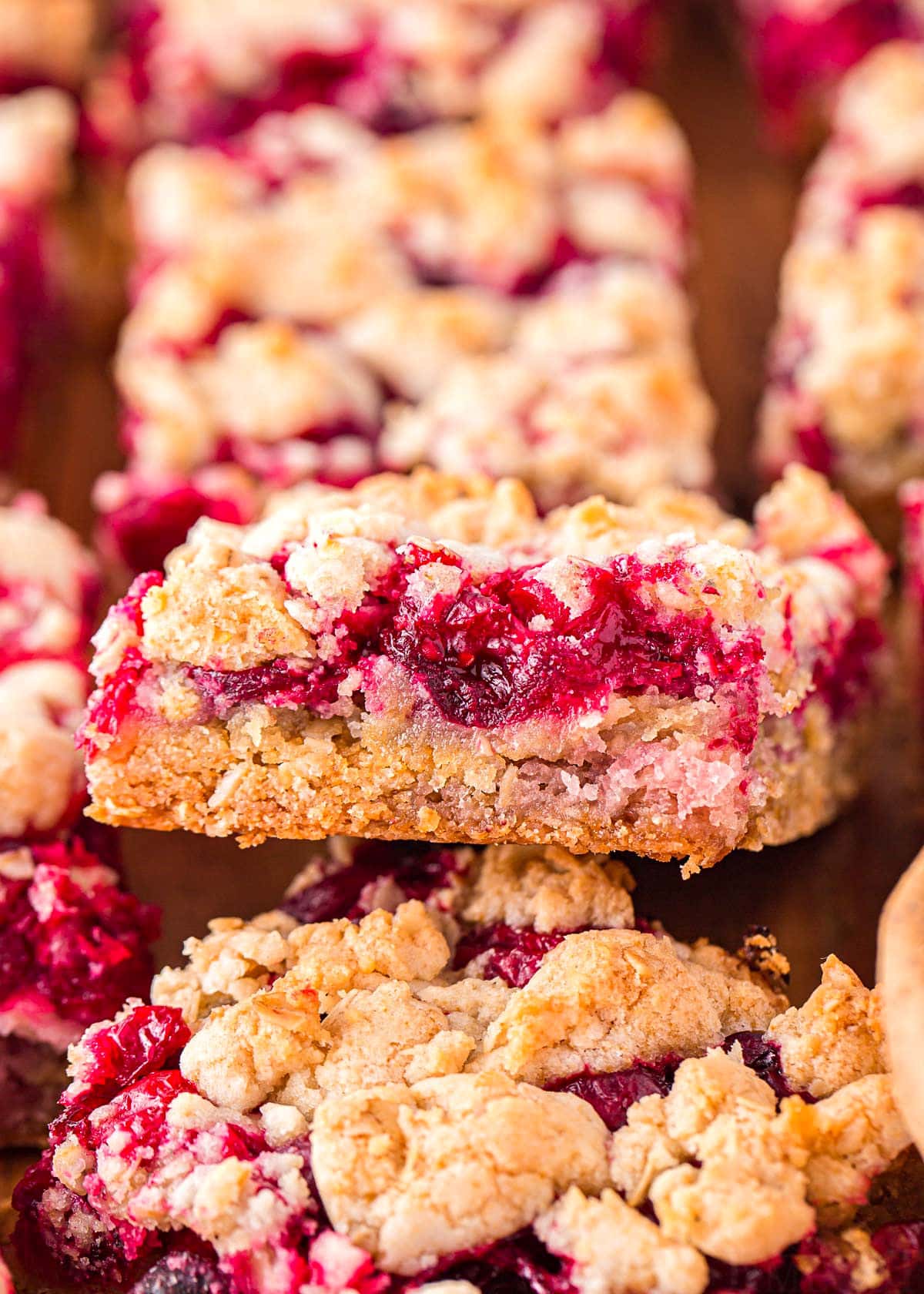 cranberry bars on a wood board with the center bar flipped up so the filling takes center stage and you can see the profile of the bar.
