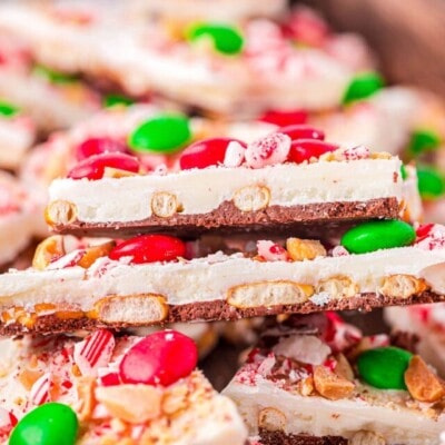 top down look at pieces of chocolate bark layered in a shallow wood tray. bark is decorated for christmas.