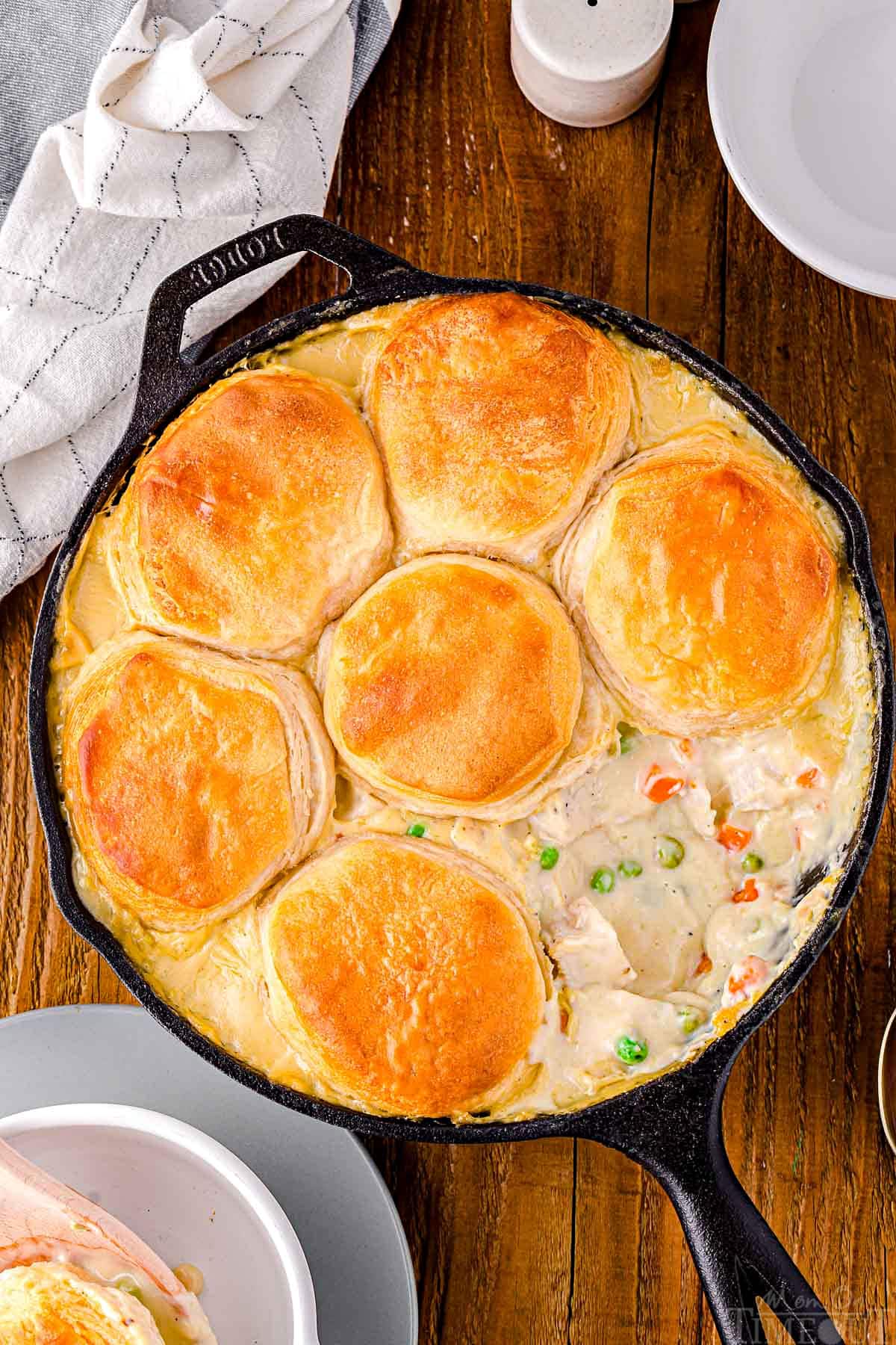 top down look at black cast iron skillet with one biscuit removed off the turkey pot pie. skillet is sitting on a wood surface.