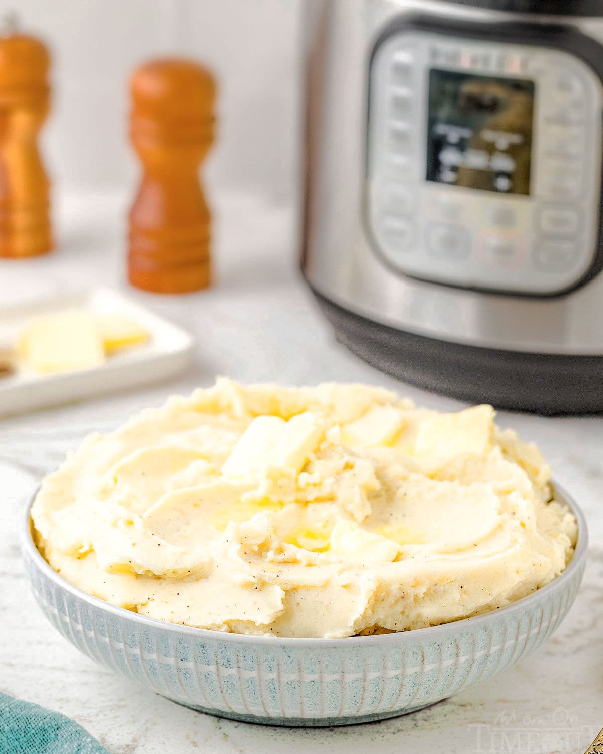 bowl of mashed potatoes sitting in front of an instant pot with salt and pepper grinders next to it.