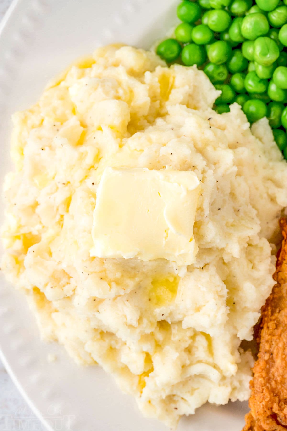 top down view of mashed potatoes on a dinner plate with peas and a piece of chicken.