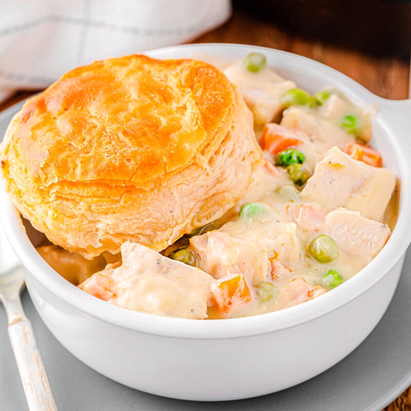 bowl filled with turkey pot pie and topped with a biscuit. the rest of the pot pie can be seen in the cast iron skillet in the background.