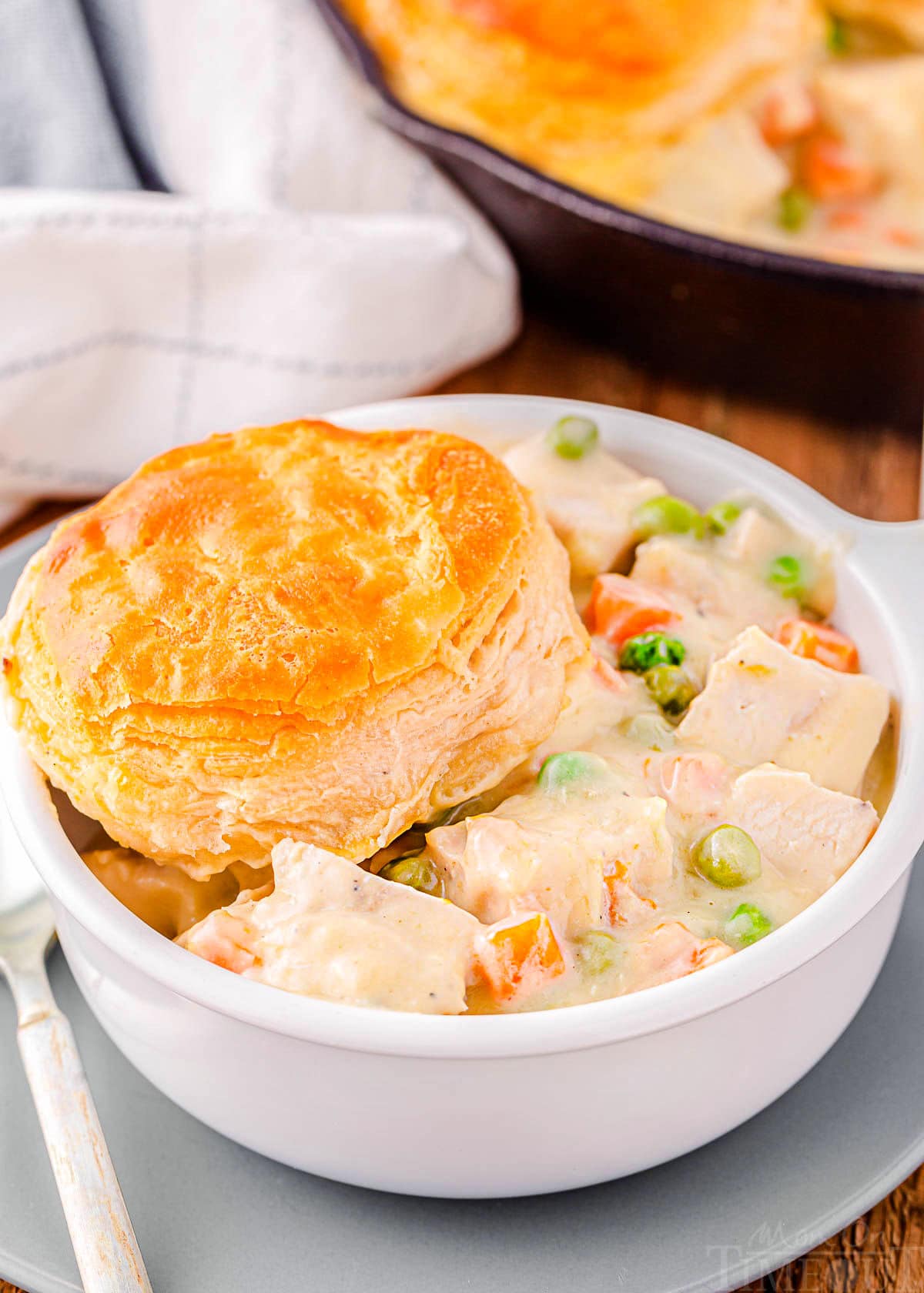 bowl filled with turkey pot pie and topped with a biscuit. the rest of the pot pie can be seen in the cast iron skillet in the background.