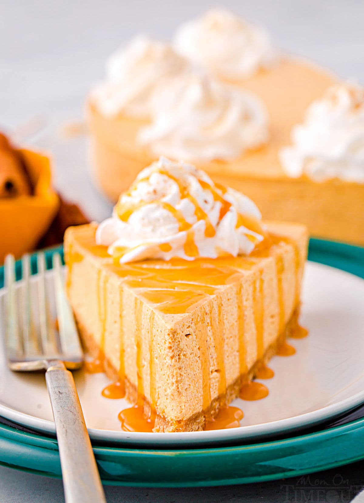 piece of pumpkin cheesecake sitting on two plates, one white and one green. the cheesecake is topped with whipped cream and a drizzle of caramel.