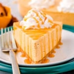 piece of pumpkin cheesecake sitting on two plates, one white and one green. the cheesecake is topped with whipped cream and a drizzle of caramel.