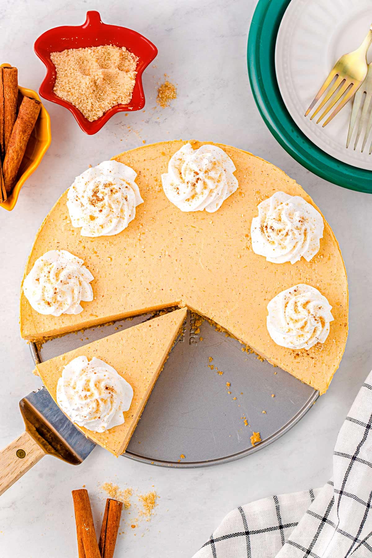 top down look at no bake pumpkin cheesecake with whipped cream dollops. one slice has been removed and another cut and ready to be served.