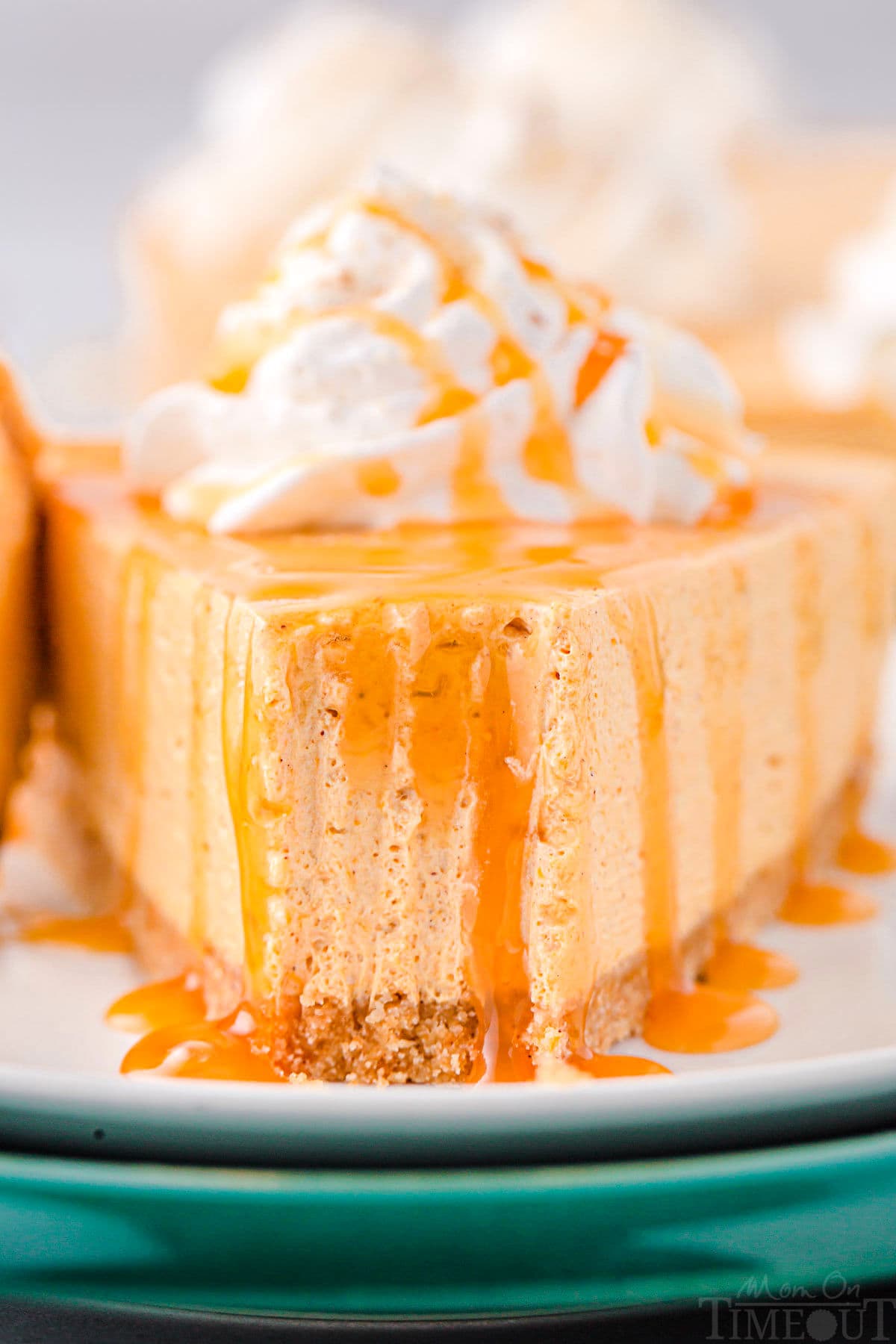 piece of pumpkin cheesecake on plate with one bite removed and you can see the marks the fork left in the cheesecake slice. the cheesecake is topped with whipped cream and caramel sauce.