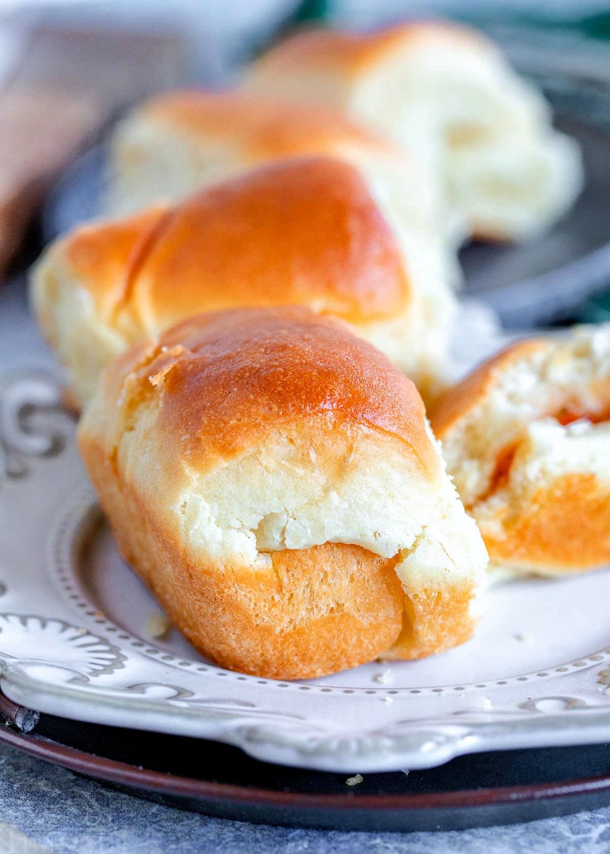 a couple rolls on a white plate with more rolls in background along with a roll that has butter and jelly and is half eaten.