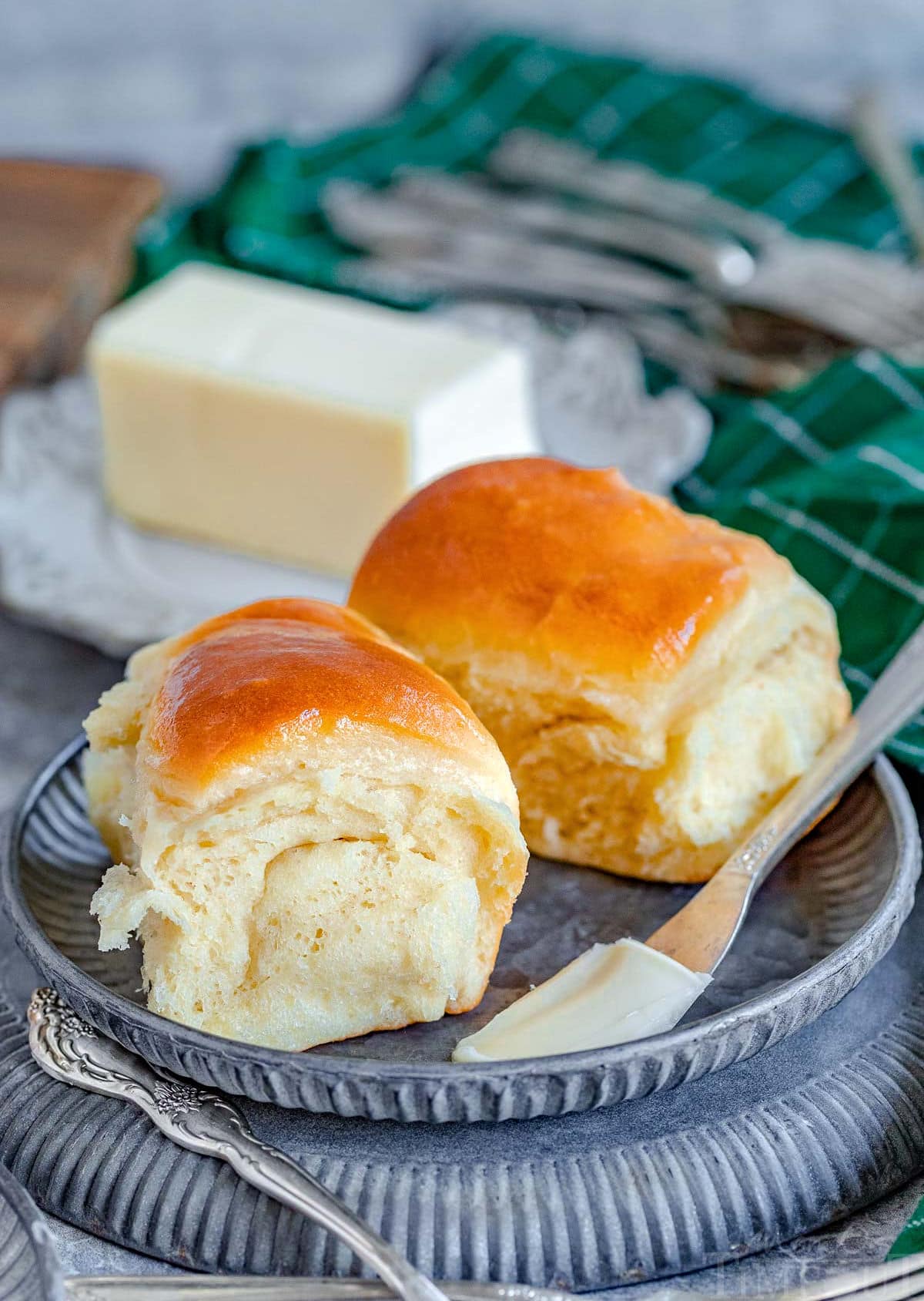two parker house rolls on a small metal plate with a stick of butter in the background.