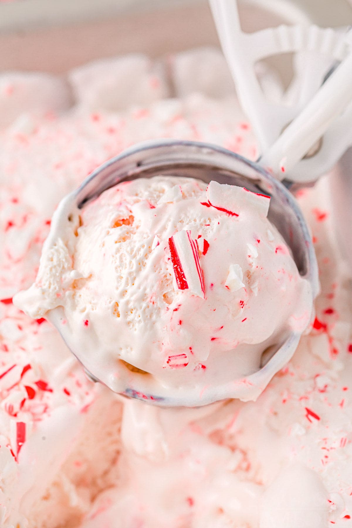 ice cream scoop filled with a scoop of peppermint ice cream held above ice cream container.