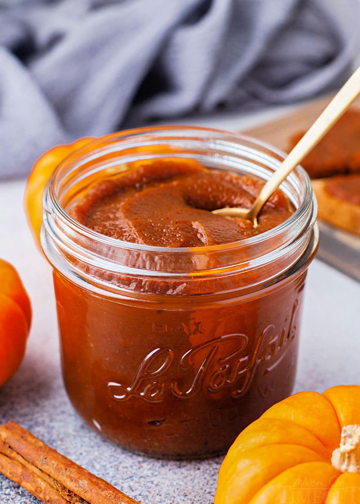 jar of pumpkin butter with small gold spoon sitting in front of a blue napkin. small pumpkin and cinnamon stick are near the jar.