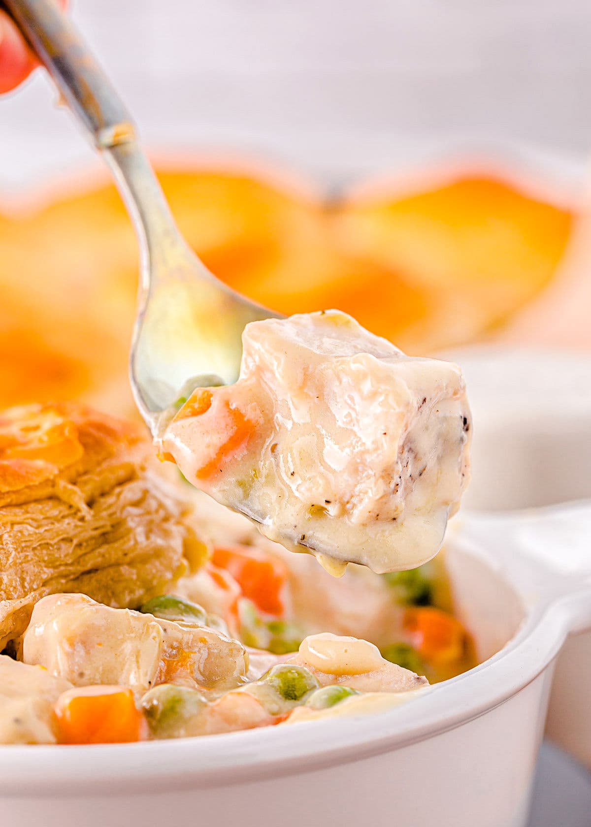 forkful of turkey pot pie being lifted out of a white bowl with biscuit topping seen in the background.