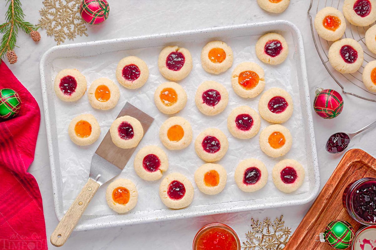 thumbprint cookies on a parchment lined baking sheet with spatula lifting off one cookie.