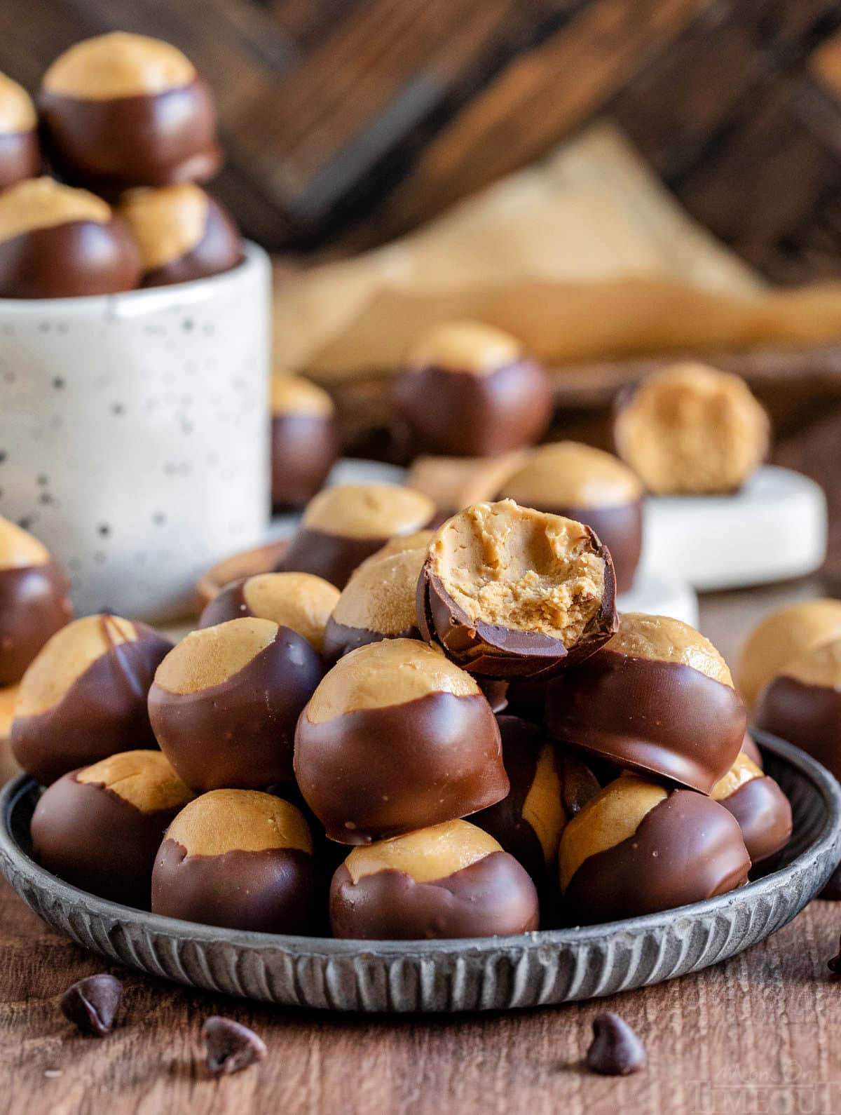 buckeyes on a silver plate with one of the candies having a bite taken, and also in a white mug. more candies are scattered about.