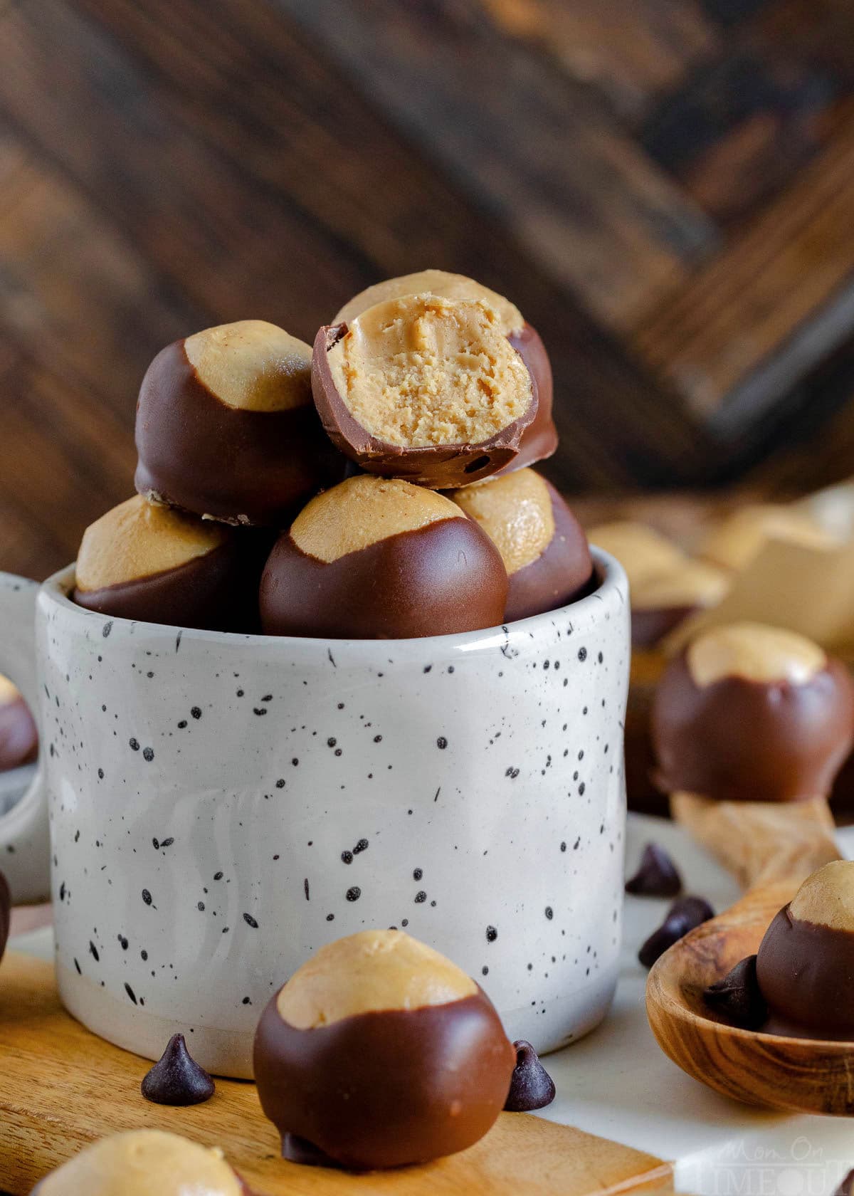 white mug filled with buckeye candy sitting on a marble cutting board with more buckeyes seen in the background and up front as well. top buckeye in mug has a bite taken out of it.