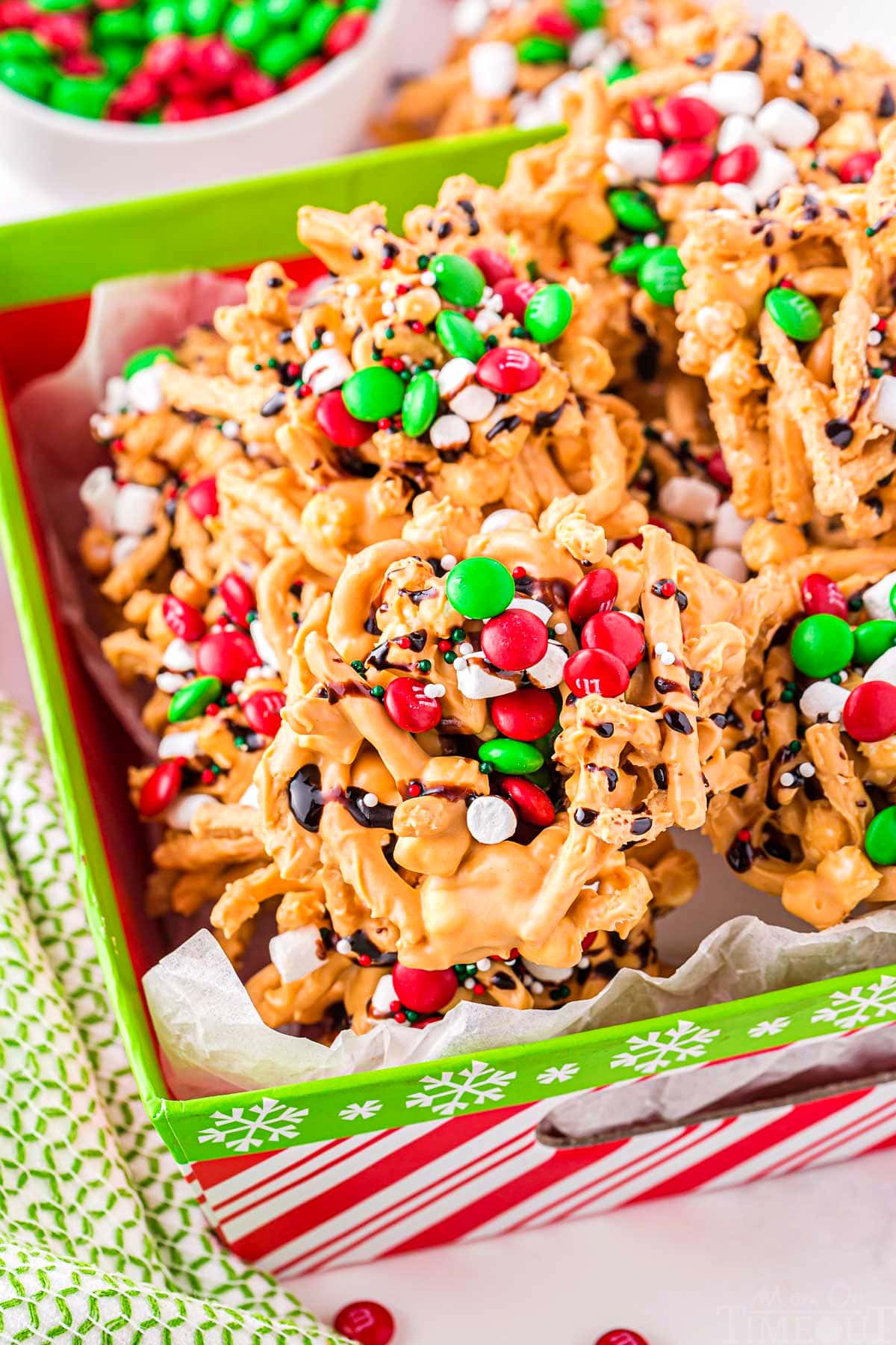 haystacks topped with candy and marshmallows sitting in a red and green Christmas box. 