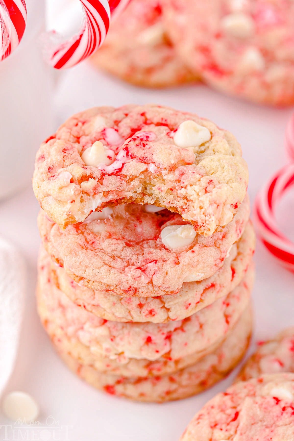 peppermint cookies stacked five high with the top cookie having a bite taken. more cookies and candy canes can be seen in the background.