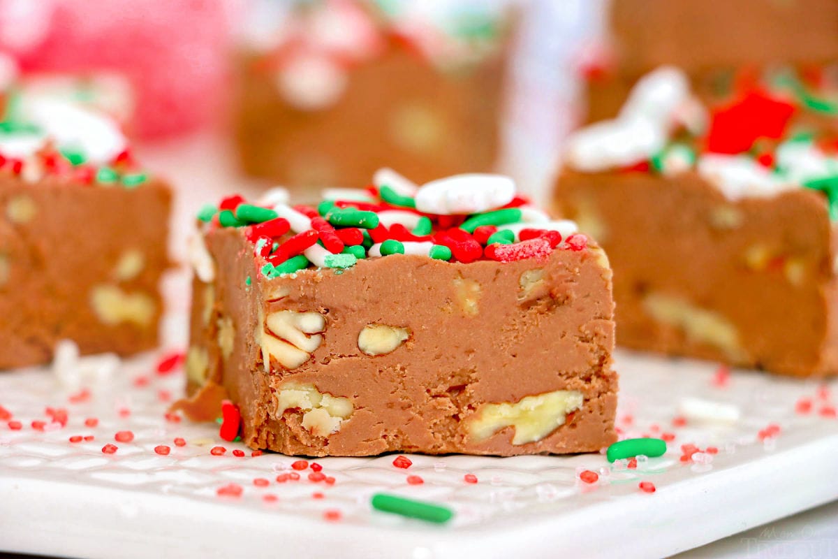 several pieces of chocolate fudge sitting on a white board with red, white and green christmas sprinkles scatter about.