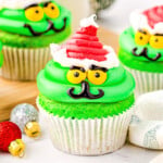 grinch cupcakes decorated with bright green frosting and a red santa hat in white cupcake liners.