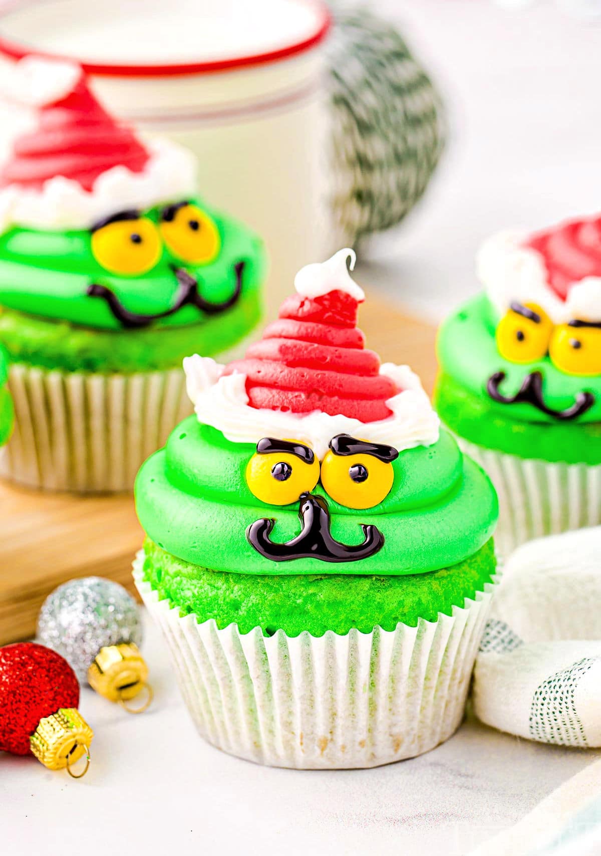 christmas cupcakes decorated like the grinch with red santa hat.