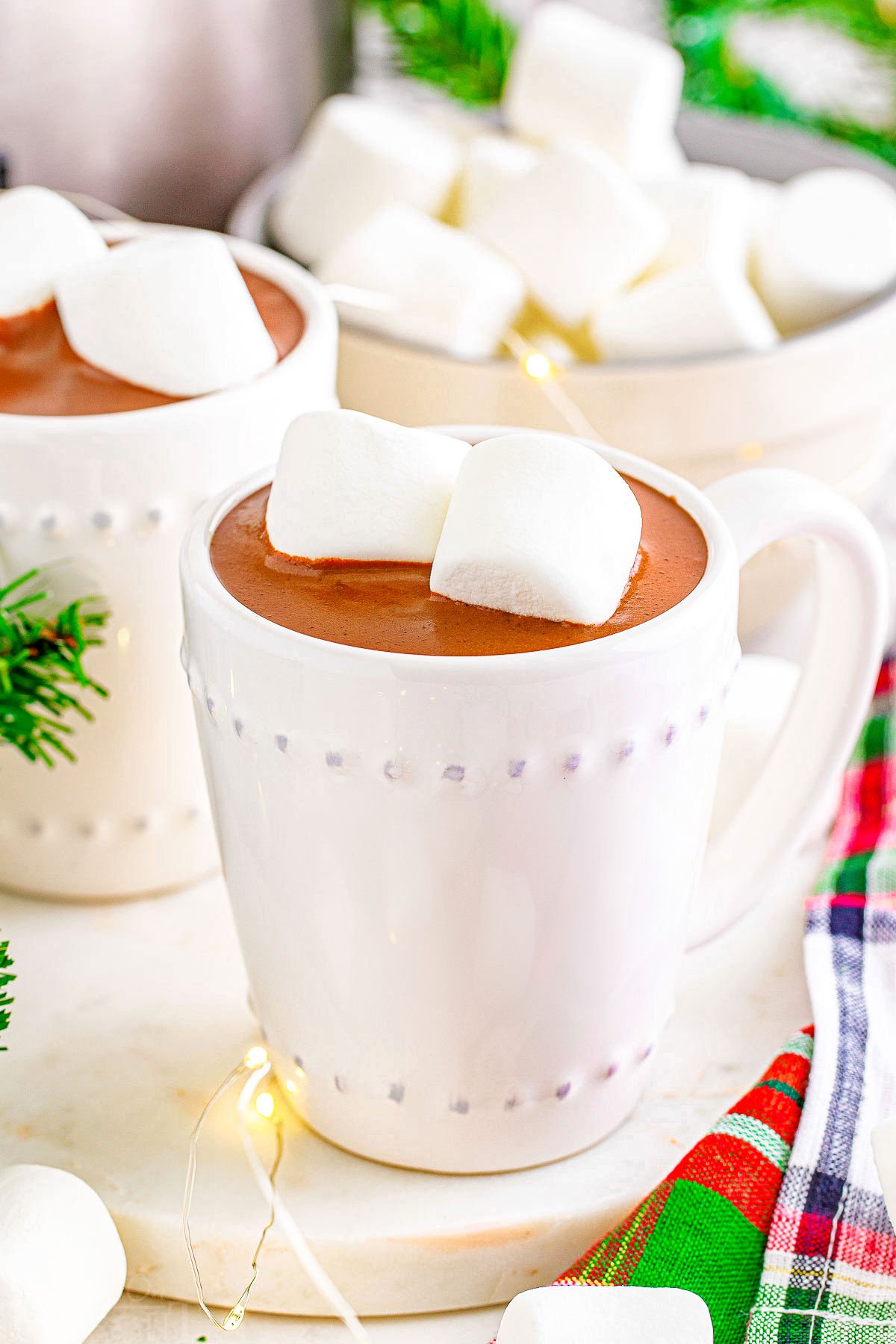 white mug filled with hot chocolate and topped with marshmallows sitting in front of another mug of crockpot hot cocoa.